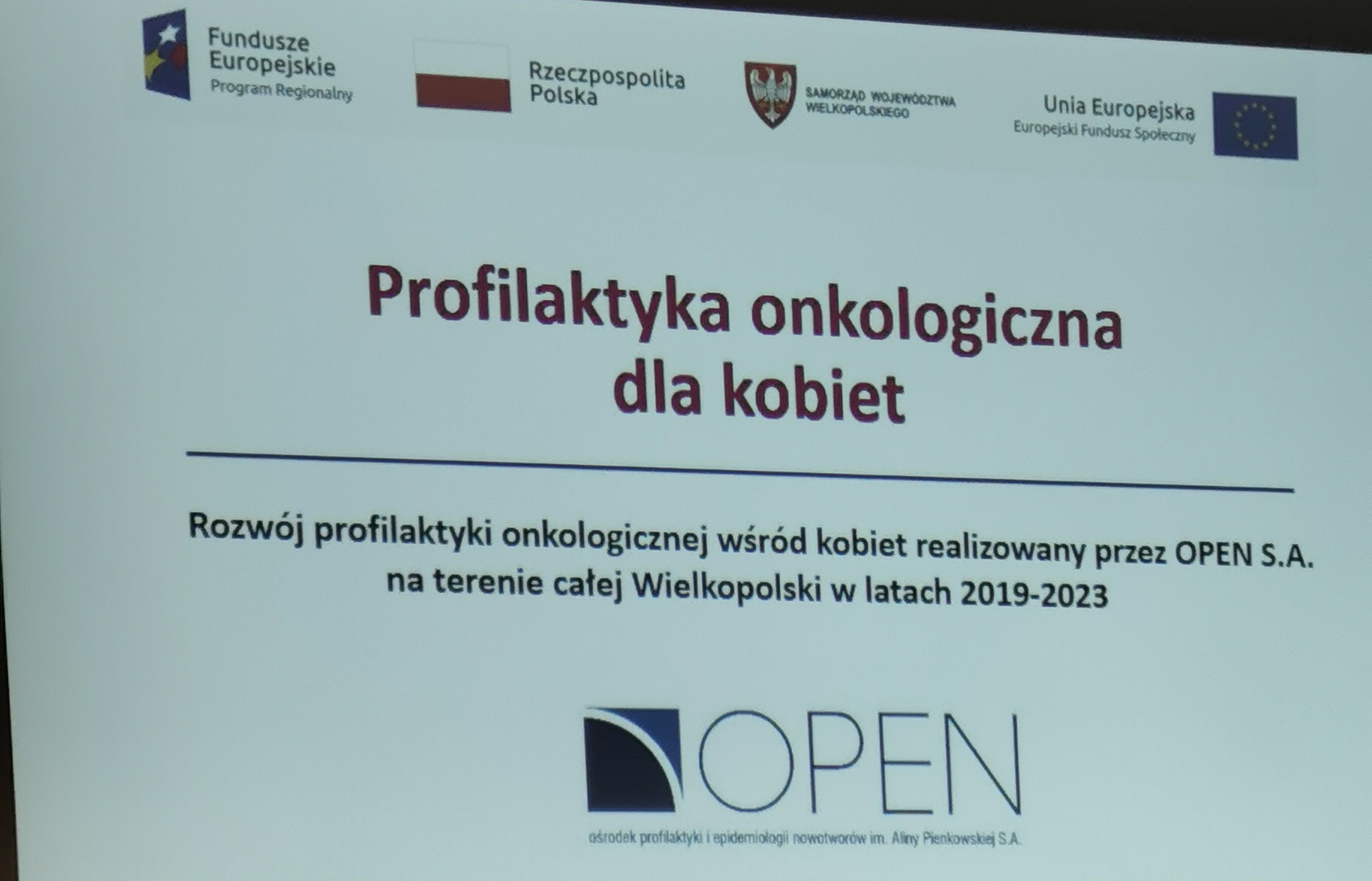 Grafika informacyjna mówiąca o profilaktyce onkologicznej dla kobiet. Jest na niej tekst mówiący o tym że OPEN S.A. na ternie Wielkopolski zajmuje się jej rozwojem w latach 2019-2023.U góry strony widać loga: Funduszu Europejskiego, RP, Samorządu Województwa Wielkopolskiego i Uni Europejskiej. A na dole strony logo organizacji OPEN