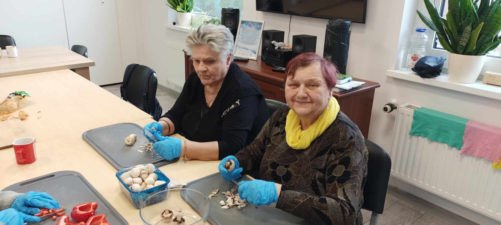 Kobiety siedzą przy stole i kroją warzywa, paprykę i pieczarki