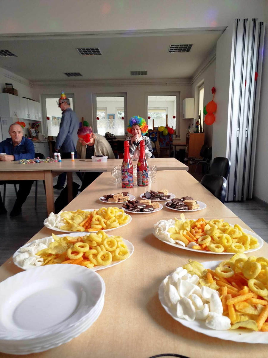 Talerze z przekąskami, ciastkami i owocami ustawione na stole podczas spotkania integracyjnego. W tle siedzące osoby