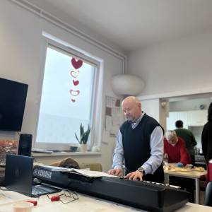 Mężczyzna operuje sprzętem muzycznym. Przed nim na stole leży laptop oraz klawiatura