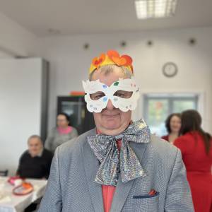 Uczestnik ŚDS w karnawałowej kreacji, w białej masce i żółtej koronie z pomarańczowo-czerwonymi sercami z papieru