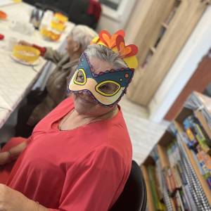 Uczestniczka ŚDS w karnawałowej kreacji, w kolorwej masce i żółtej koronie z pomarańczowo-czerwonymi sercami z papieru