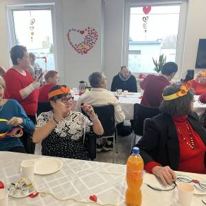 Uczestnicy ŚDS siedzą przy długich zastawionych stołach. Na ścianach i oknach widać walentynkowe ozdoby w kształcie serc