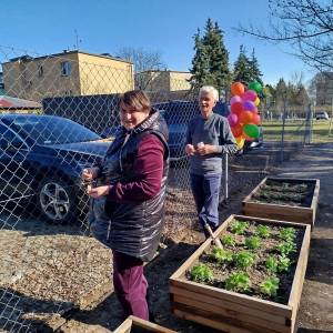 Dwóch uczestników ŚDS pozuje do zdjęcia przy dwóch skrzyniach wypełnionymi posadzonymi roślinkami