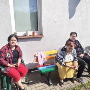 Uczestniczki ŚDS siedzą na kolorowej ławce pod ścianą budynku ŚDS