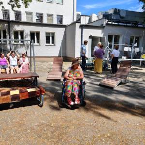 Uczestnicy ŚDS i pracownicy Centrum Usług Społecznych w Swarzędzu w ogrodzie społecznym. Niektórzy siedzą, inni rozmawiają między sobą