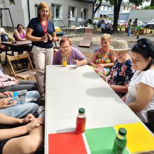 Uczestnicy ŚDS biorą udział w zabawie siedząc przy stole na ogrodzie Centrum Usług Społecznych