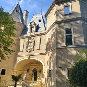 Zabytkowy dziedziniec Zamku w Gołuchowie z widokiem na renesansową architekturę rezydencji, strzeliste wieżyczki ze spiczastymi dachami oraz zdobioną kamienną fasadę ze sztukateriami. Na parterze widoczne są reprezentacyjne arkady, ozdobne kamienne schody z tralkową balustradą oraz turyści wchodzący do wnętrza zamku. Zdjęcie zostało wykonane w pełnym słońcu podczas wspólnej wycieczki zorganizowanej przez Dzienny Dom „Senior-Wigor” w Swarzędzu oraz Środowiskowy Dom Samopomocy.