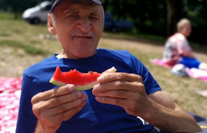 Starszy mężczyzna siedzi na plaży i pozuje do zdjęcia jedząc arbuza