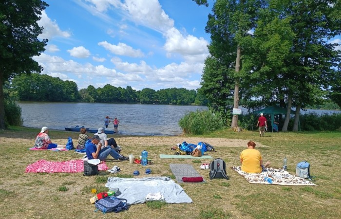 Na kocach siedzą osoby, korzystają z dobrej pogody spędzając czas przy jeziorze