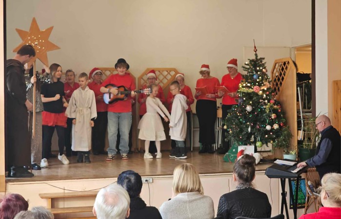 Kolędnicy na scenie a przed nimi scenka odgrywana, chłopak gra na gitarze dwie pary dzieci tańczą 