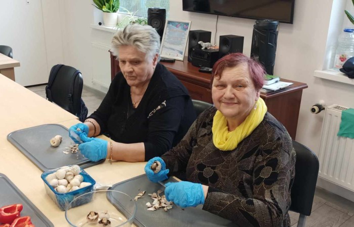 Kobiety siedzą przy stole i kroją warzywa, paprykę i pieczarki 