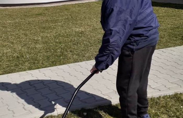 Ciepło ubrany starszy pan grabi suche igły i liście z trawnika przed budynkiem