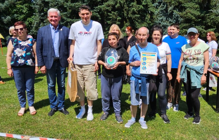 Drużyna pozuje do zdjęcie po wyręczeniu nagród, trzy osoby pośrodku trzymają kolejną papierową torbę z czymś w środku, statuetkę i dyplom