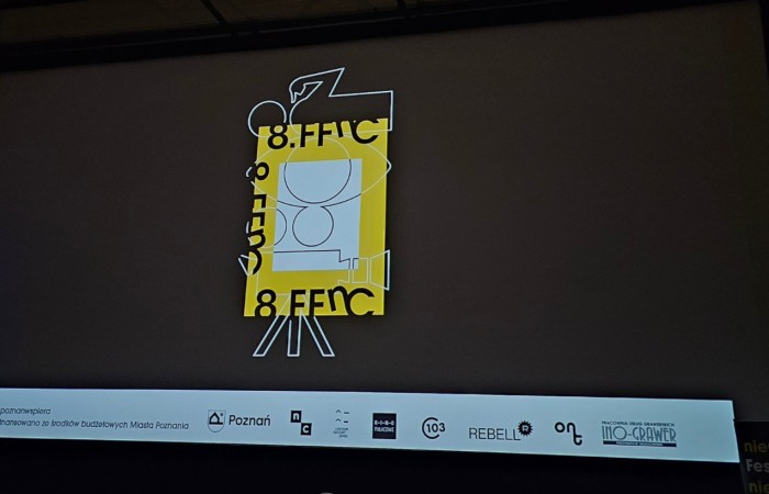 Logo 8. FFnC na czarnym tle, kamera, oko i człowiek narysowane prostą białą kreską, W białym kwadracie z grubym żółtym obramowaniem  