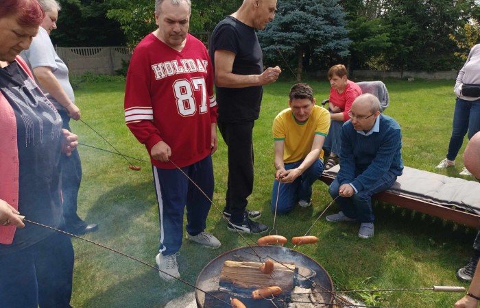 Osoby pieką nabite na kijki kiełbaski nad ogniskiem 