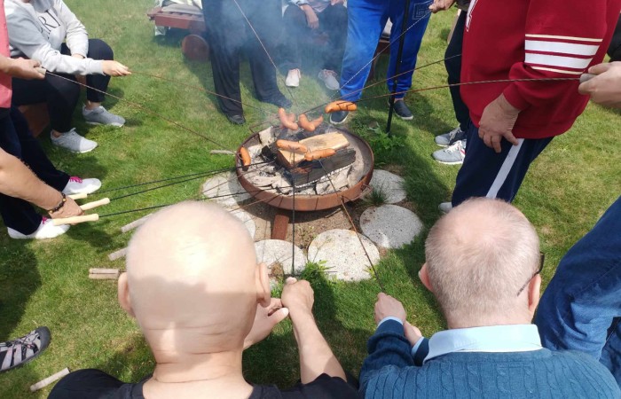 Osoby pieką nabite na kijki kiełbaski nad ogniskiem 