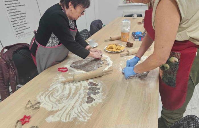 Dwie starsze kobiety rozwałkowują ciasto i wykrawają foremkami różne kształty pierników