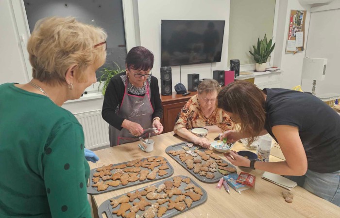 Cztery kobiety ozdabiają pierniki na tackach, pisakami, lukrem i posypkami. 