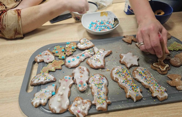 Cztery kobiety ozdabiają pierniki na tackach, pisakami, lukrem i posypkami