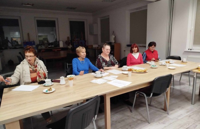 Grupa osób siedzi przy długim stole, z filiżankami i talerzykami.