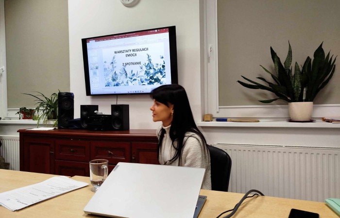 Młoda kobieta wyświetla prezentację na telewizorze, tematem są warsztaty regulacji emocji.