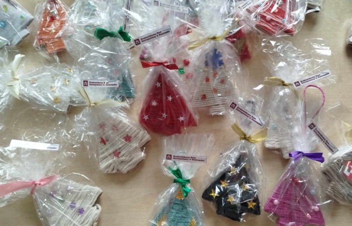 Ciasteczka w przezroczystych opakowaniach ozdobionych kolorowymi wstążkami. Ciasteczka mają różne kolory i kształty, np. choinek i dzwoneczków