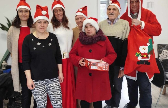 Zdjęcie grupowe siedmiu osób ubranych w czapki świętego Mikołaja. Niektóre osoby mają na sobie czerwone ubrania lub akcenty świąteczne, a jedna osoba trzyma prezent