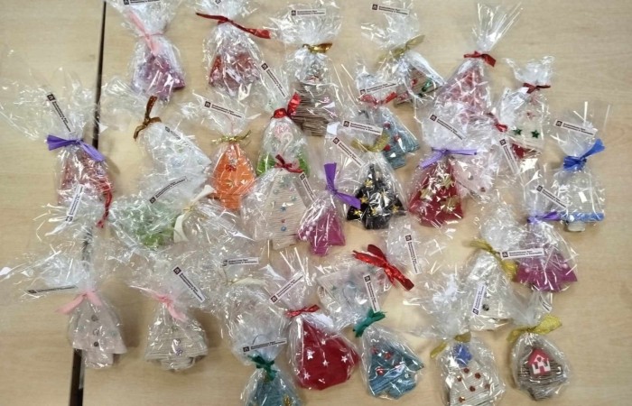 Ciasteczka w przezroczystych opakowaniach ozdobionych kolorowymi wstążkami. Ciasteczka mają różne kolory i kształty, np. choinek i dzwoneczków