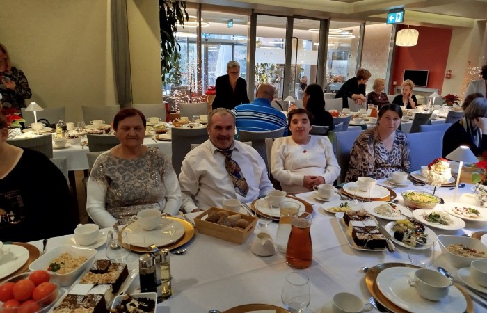 Kilka osób siedzących przy elegancko nakrytym stole w trakcie uroczystego spotkania. W tle widoczni są pozostali uczestnicy