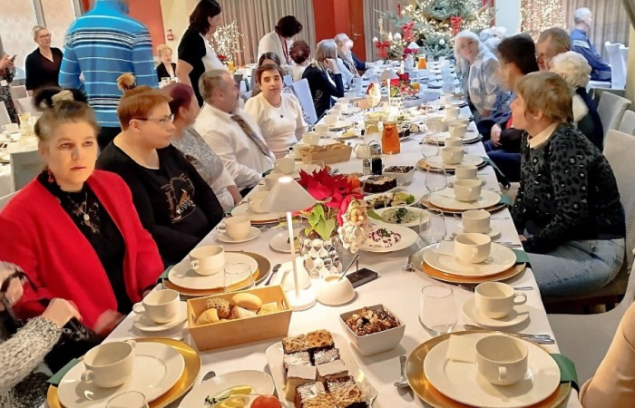 Grupa osób siedzących przy długim stole, zastawionym elegancką zastawą i różnymi przekąskami podczas uroczystości