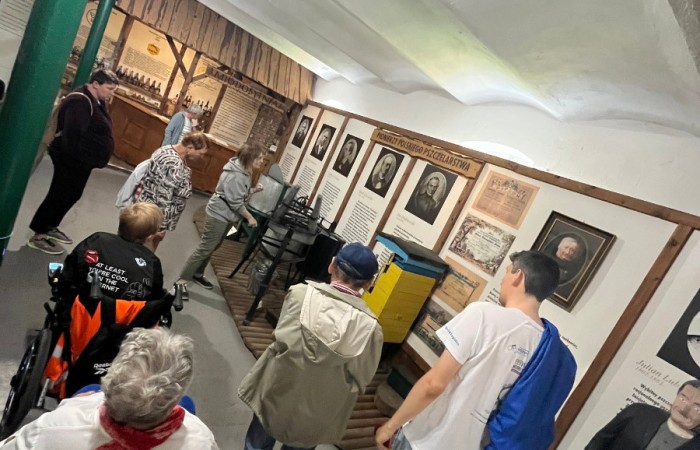 Uczestnicy ŚDS wraz z przewodnikiem zwiedzają muzeum, podziwiając stoisko z pionierami polskiego pszczelarstwa