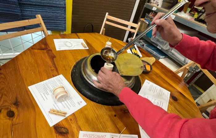 Uczestnicy ŚDS pobierają chochlą rozgrzany wosk z metalowej pojemnika, i przelewają go do gotowej formy na świeczkę